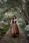 Schwere Hexe in Kleid steht mit Besen auf Straße im Wald und blickt in Kamera — Stockfoto