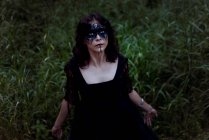 Von oben die mystische Hexe im langen schwarzen Kleid und mit aufgemaltem Gesicht, die in dunklen, düsteren Wäldern aufblickt — Stockfoto