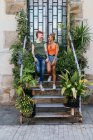 Содержание молодой татуированной женщины, разговаривающей с возлюбленной гомосексуалиста, глядя друг на друга, стоящей на лестнице между растениями — стоковое фото