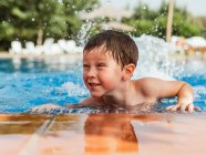 Deleitado niño lindo con el pelo mojado apoyado en la piscina mientras se divierten durante el fin de semana de verano - foto de stock