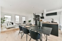 Esstisch mit Stühlen und Küche mit schwarzen Schränken in der Nähe Wohnbereich mit Topfpflanzen dekoriert — Stockfoto