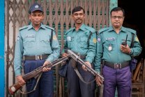INDIA, BANGLADESH - DECEMBER 6, 2015: Етнічні озброєні чоловіки в поліцейській уніформі одяг і шапка стоять біля металевих брам вивітрювання будівлі і дивляться на камеру — стокове фото