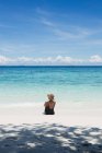 Back view female tourist in swimsuit and straw hat sitting in transparent sea during trip in Malaysia — Stock Photo