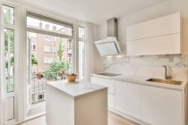 Интерьер просторной кухни со стильной светлой мебелью в роскошных современных апартаментах в дневное время — стоковое фото