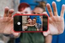Весёлые гомосексуальные женщины с татуировками, снимающие автопортрет по мобильному телефону у входной двери в городе — стоковое фото
