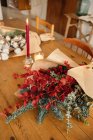 Desde arriba de fiesta elegante ramo de Navidad decorativo con ramitas de eucalipto y ramas de color rojo brillante con bayas colocadas en la mesa de madera con velas en la habitación - foto de stock