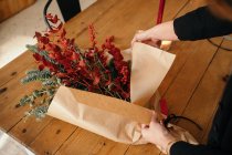 From above of crop unrecognizable female florist standing at wooden table arranging Christmas bouquet in room — Stock Photo