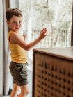 Bambino sereno in piedi vicino alla finestra in cottage e guardando lontano nei pensieri — Foto stock