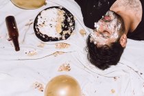 De cima do homem bêbado dormindo perto de bolo de aniversário esmagado e garrafa vazia durante a festa — Fotografia de Stock