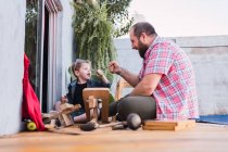 Ground level of cheerful bearded dad in checkered shirt against boy bumping fists while looking at each other against wooden blocks — Stock Photo