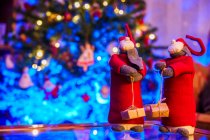 Gnomos de juguete suave para la celebración de Navidad colocados en la mesa contra el árbol festivo borroso decorado con guirnaldas brillantes - foto de stock