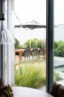 Interieur des Zimmers mit Fenster mit Blick auf die Terrasse mit grünen Pflanzen und Holztisch am Tag — Stockfoto