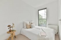 Интерьер просторной светлой спальни с удобной кроватью и большими окнами в современной квартире днем — стоковое фото