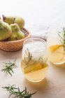 From above of cold pear cocktail in glasses with rosemary and ice cubes placed on table with fresh fruits — Stock Photo