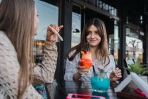 Crop content migliori amiche con gustose bevande e spuntini parlando mentre si guardano in caffetteria di strada — Foto stock