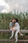 Side view of charming young homosexual girlfriends spending time on fence under cloudy sky in evening countryside — Stock Photo