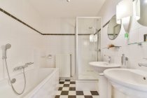 Design criativo do banheiro com lâmpada entre lavatórios contra banho em forma retangular no piso de azulejos em casa — Fotografia de Stock