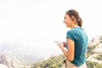 Vue latérale de textos touristiques féminines positives sur téléphone portable lors d'une excursion dans les montagnes de Montserrat en Espagne — Photo de stock