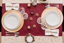 Vista dall'alto della tavola apparecchiata con bicchieri e posate vicino a piatti decorati con candele e coni per la celebrazione del Natale — Foto stock