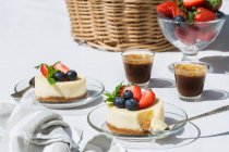 Gâteaux au fromage sucré savoureux aux myrtilles et fraises servis sur une table en verre près des tasses de café — Photo de stock