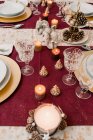 Von oben vom Banketttisch mit Geschirr und Gläsern serviert und mit brennenden Kerzen und Zapfen für das Weihnachtsessen dekoriert — Stockfoto
