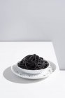 Минималистская студия с черными чернилами кальмара спагетти в полной керамической миске на белом столе — стоковое фото