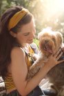 Vue latérale de heureux propriétaire féminin souriant largement tout en appréciant le temps avec Yorkshire Terrier drôle avec la langue sur — Photo de stock