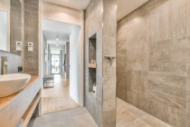 Интерьер стильной чистой ванной комнаты с серой плиткой стен и в современных апартаментах — стоковое фото
