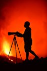 Vue latérale de la silhouette d'un homme enregistrant et photographiant avec un téléobjectif et trépied l'explosion de lave sur La Palma Canaries 2021 — Photo de stock