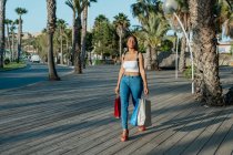 Allegro giovane acquirente afro-americano femminile con borse della spesa guardando lontano mentre camminava per strada — Foto stock