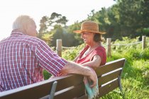 Seitenansicht eines älteren Ehepaares, das sich auf einer Holzbank anschaut und den Sommertag am Ufer des Teiches genießt — Stockfoto