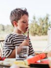 Орієнтована чарівна дитина розмазає масло на скибочці хліба, снідаючи за столом у дворі влітку — стокове фото
