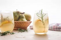 Cocktail di pere fredde in bicchieri con rosmarino e cubetti di ghiaccio disposti sul tavolo con frutta fresca — Foto stock