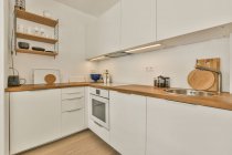 Interior da cozinha com móveis brancos e balcão de madeira e elementos no apartamento moderno — Fotografia de Stock