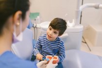 Усмішка жінки - ортодонта навчає пацієнта зубною щіткою чистити зуби за моделлю щелепи в стоматологічній клініці — стокове фото