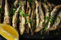 Vista aérea de las apetitosas anchoas fritas con perejil picado y rodaja de limón fresco con carne jugosa - foto de stock