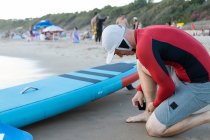 Вид сбоку серфера-мужчины в гидрокостюме, который вставляет лодыжку в доску SUP во время подготовки к погружению для серфинга на берег моря — стоковое фото