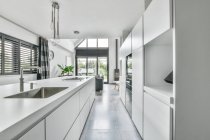 Светлый интерьер кухни с металлической раковиной и встроенной бытовой техникой в современном доме — стоковое фото