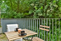 Petite table et chaises en bois placées sur la terrasse contre les arbres verts en journée — Photo de stock