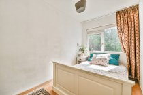 Interior del acogedor dormitorio con maceta planta y cama colocada cerca de la ventana en la casa contemporánea - foto de stock