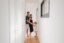 Side view of child caressing belly of smiling expectant mother against dad while looking at camera in passage at home — Stock Photo