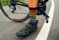 Nível do solo de atleta masculino sem rosto em sapatos de ciclismo e meias listradas em pé na estrada com bicicleta — Fotografia de Stock