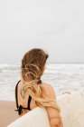 Вид ззаду на невідому молоду спортсменку в купальнику з дошкою для серфінгу, яка дивиться на піщане узбережжя проти штормового океану — стокове фото