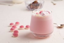 Bicchiere di cioccolato bianco caldo dolce con caramelle alla gelatina rosa e marshmallow servito su tavolo bianco — Foto stock