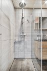 Интерьер современной ванной комнаты с душевой кабиной и раковиной выполнен в минимальном стиле с серой плиткой — стоковое фото