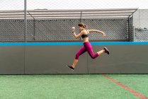 Full body of enduring female athlete in activewear jumping above ground during intense training in stadium — Stock Photo
