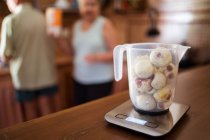 Figos maduros em jarro em balanças de pesagem com exibição na mesa contra parceiros anônimos de cultura na cozinha — Fotografia de Stock