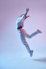 Seitenansicht einer energischen ethnischen Frau mit drahtlosen Kopfhörern und trendigen Klamotten, die mit offenen Armen springt, während sie Hip-Hop tanzt — Stockfoto
