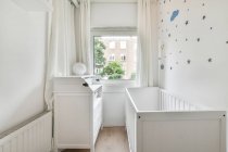 Petit lit bébé en bois placé près de la fenêtre dans la chambre à coucher avec intérieur minimaliste en journée — Photo de stock