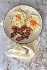 Visão aérea de ovos ensolarados saborosos com tiras de bacon fritas na placa acima da toalha — Fotografia de Stock